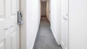A narrow hallway with white doors, a grey carpet, and a security keypad on one door. - The Nook - Room 11 - Family Room (St Ives)