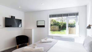 A modern bedroom with a large bed, a TV, a chair, and a window with a view of the garden. - The Nook - Room 11 - Family Room (St Ives)