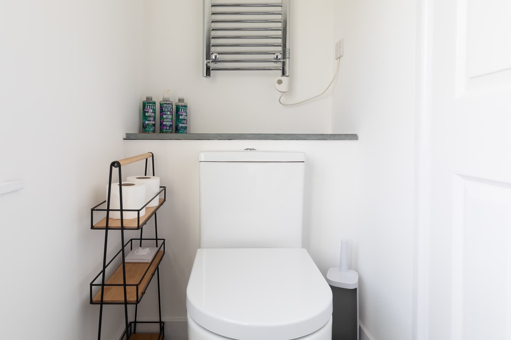 Eine weiße Toilette mit Ablage, auf der Toilettenpapier und eine Handseifenflasche liegen.