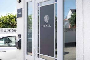 L’entrée d’un immeuble, avec une enseigne indiquant « The Nook », une porte dotée d’un panneau en verre et un clavier fixé au mur.