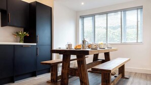 Een moderne keuken met donkere kastjes, een houten eettafel met banken en een raam met zonwering.