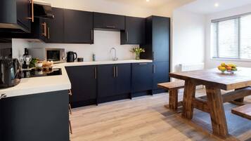 A modern kitchen with dark cabinets, a wooden dining table, and a window with blinds.