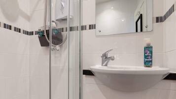 A bathroom with a glass shower enclosure, a white sink with a chrome faucet, and a bottle of hand wash soap.