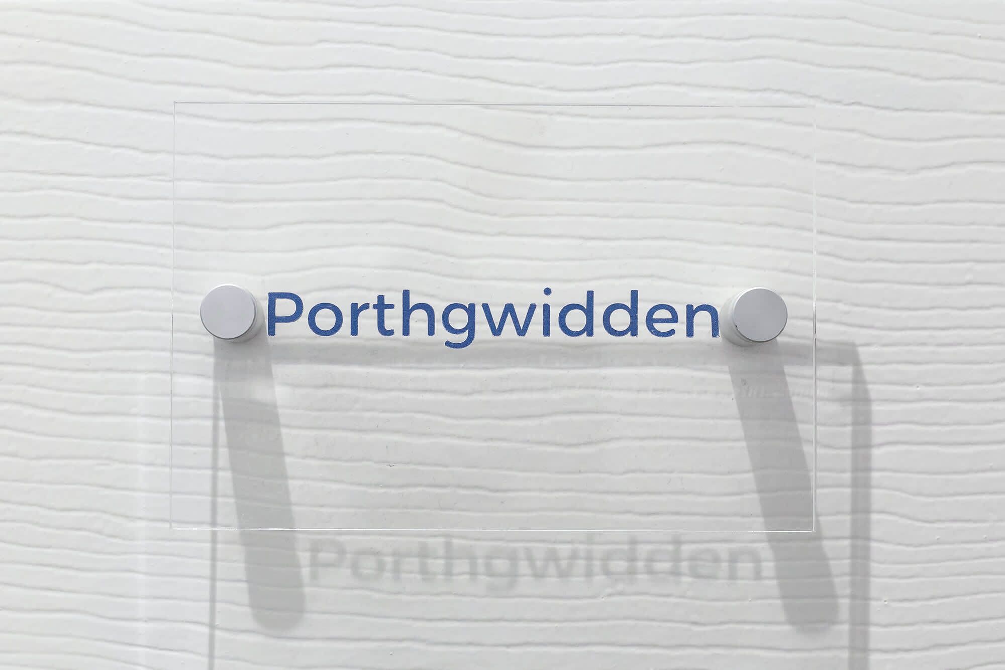 A sign with the text 'Porthgwydden' pinned to a textured wall.