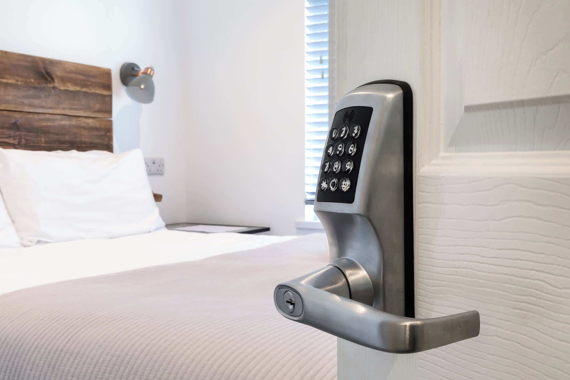 Habitación de hotel moderna con cama, mesita de noche y cerradura electrónica en la pared.