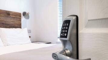 Habitación de hotel moderna con cama, mesita de noche y cerradura electrónica en la pared.