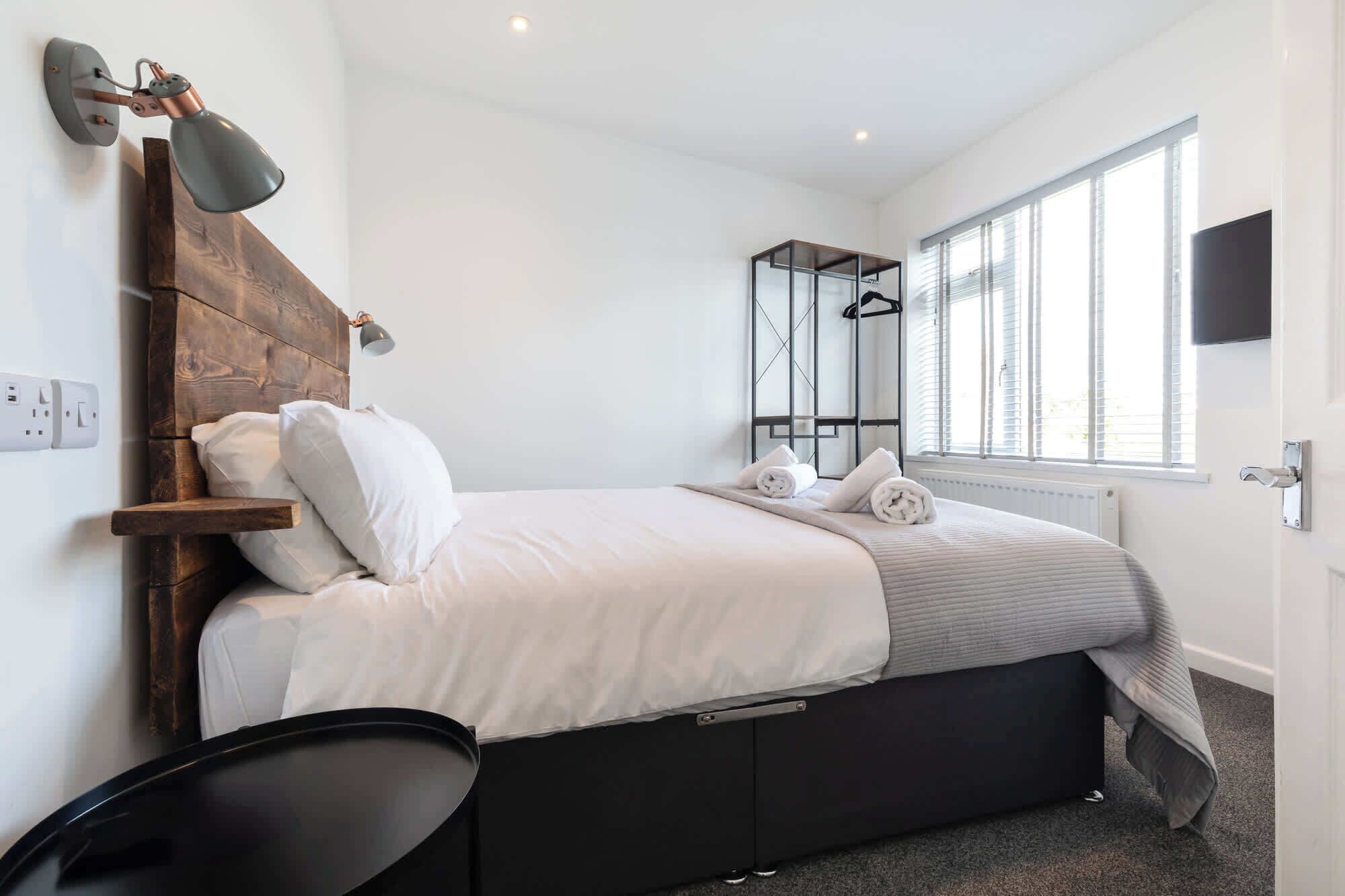 Un dormitorio con cama, lámparas de noche, un perchero y una ventana.