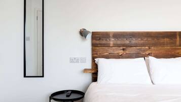 A bedroom with a wooden headboard, white bedding, a round black table, and a wall-mounted light fixture.