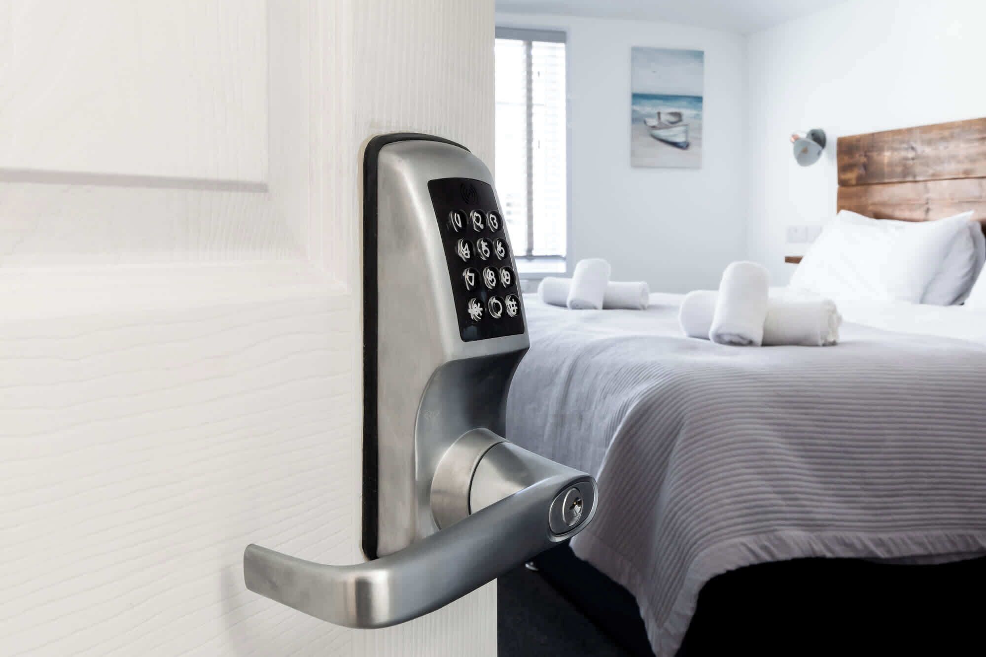 Habitación de hotel con una cerradura de puerta moderna, una cama con cubrecama a rayas y vista al océano a través de la ventana.