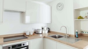 Eine moderne Küche mit weißen Schränken, einer Edelstahlspüle, einem Toaster, einem Wasserkocher und einer Wanduhr.