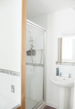 A bathroom with a glass shower enclosure, a white sink, and a mirror above it.