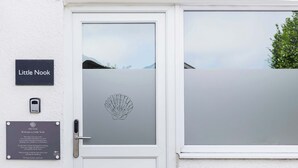 Eine weiße Tür mit einer satinierten Glasscheibe, einem Klingel und einem Schild mit der Aufschrift 'Little Nook'.