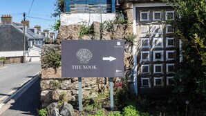 Ein Schild mit der Aufschrift 'The Nook' und einem nach rechts zeigenden Pfeil, umgeben von Steinmauern und Vegetation.