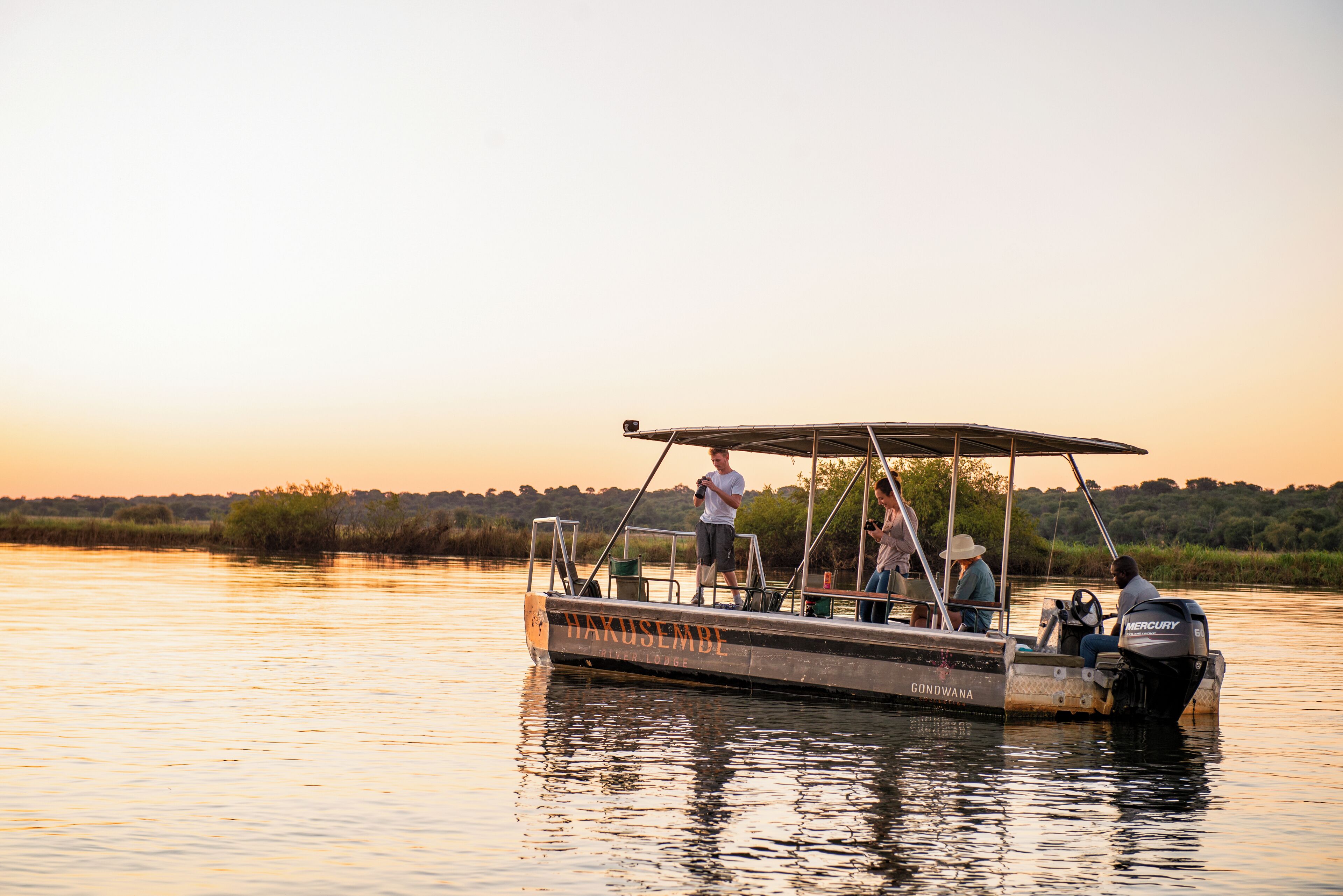 Un bote con toldo, identificado como 'Gondwana', en aguas tranquilas durante el atardecer.