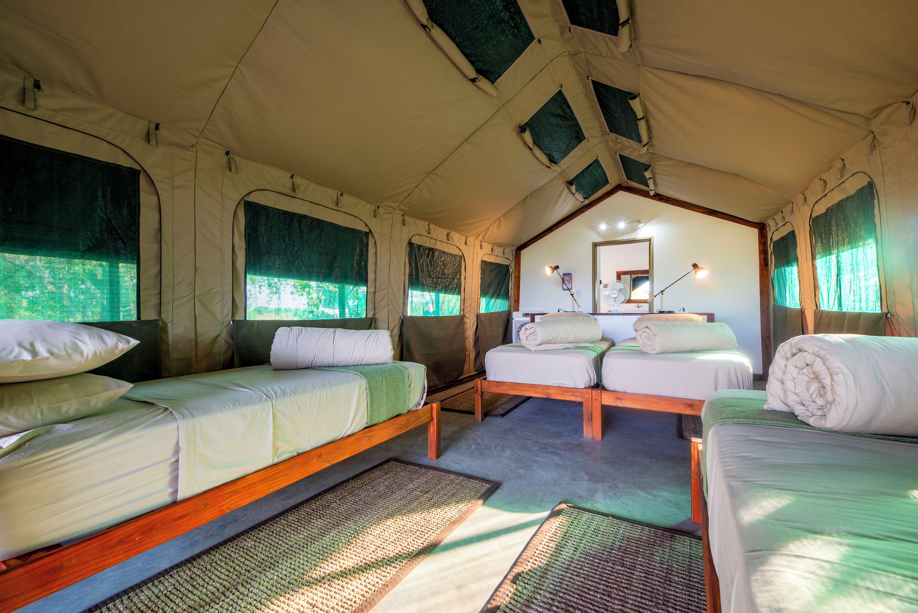 A tented accommodation with two beds, a small table, and a mirror.