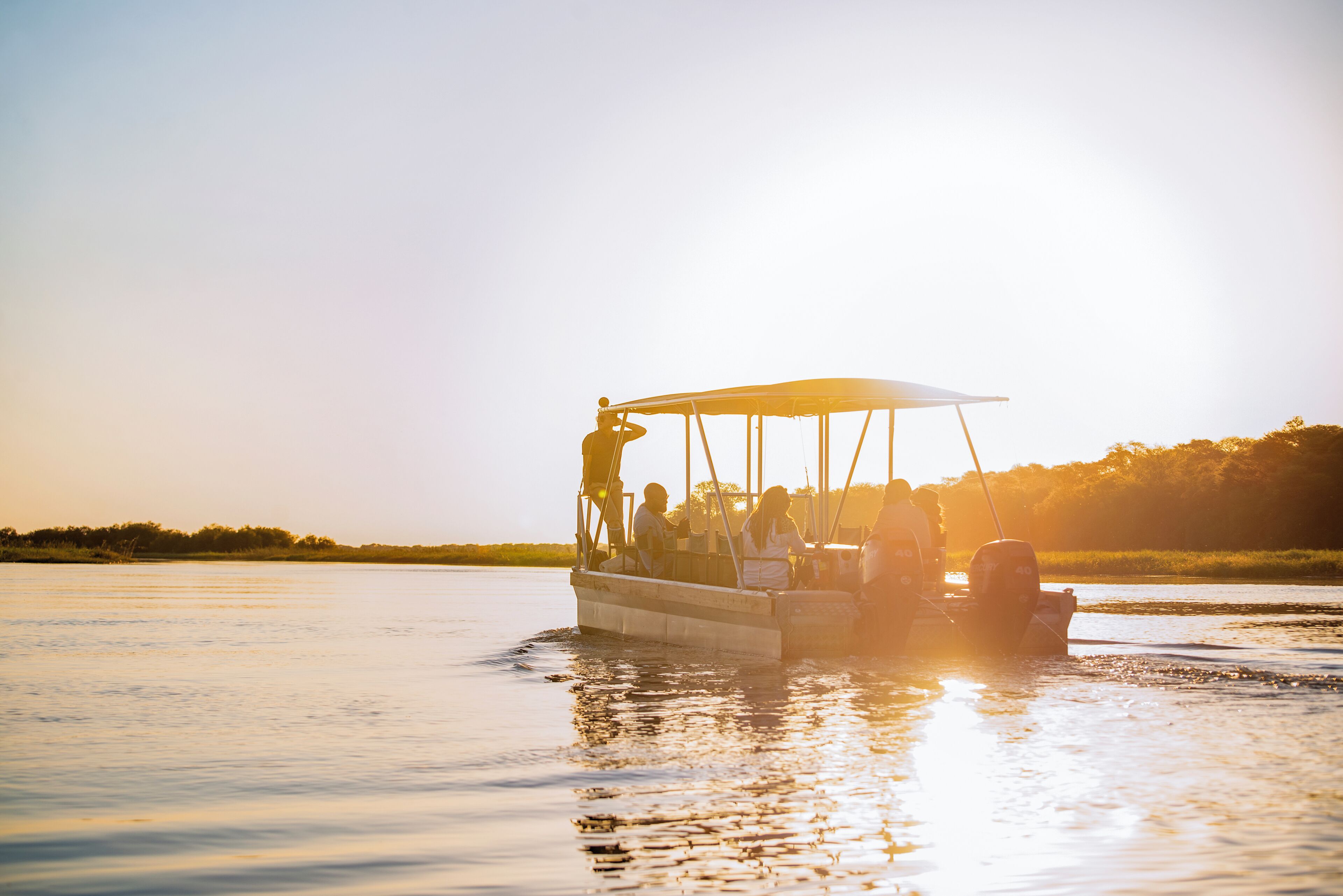 A boat with passengers, moving on calm water during sunset.
