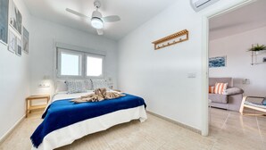 A bedroom with a bed, a ceiling fan, a window, a bedside table, and a door leading to another room. - Casa Ramé - Beachfront with AACC By LVH (Puerto del Carmen)