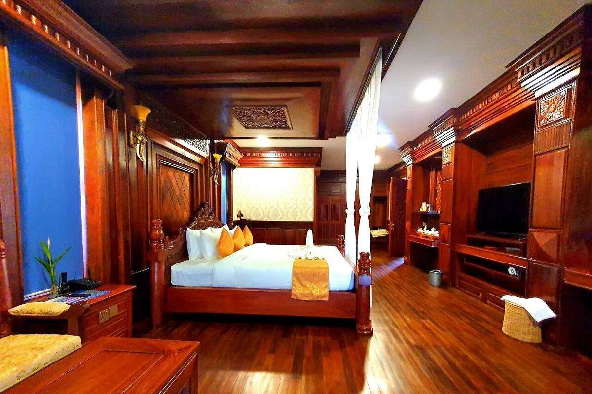 Een ruime slaapkamer met een groot bed, houten meubels en een televisietoestel.
