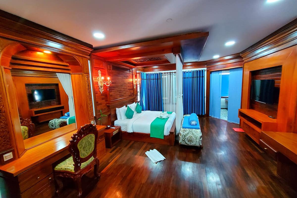 Ein Hotelzimmer mit Holzboden, einem Bett mit grünen Kissen, einem Fernseher, einem Sessel und einem kleinen Tisch.