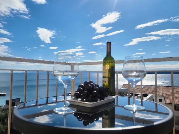 Une table avec deux verres à vin, une bouteille de vin et un bol de raisins, le tout placé devant un paysage marin pittoresque.