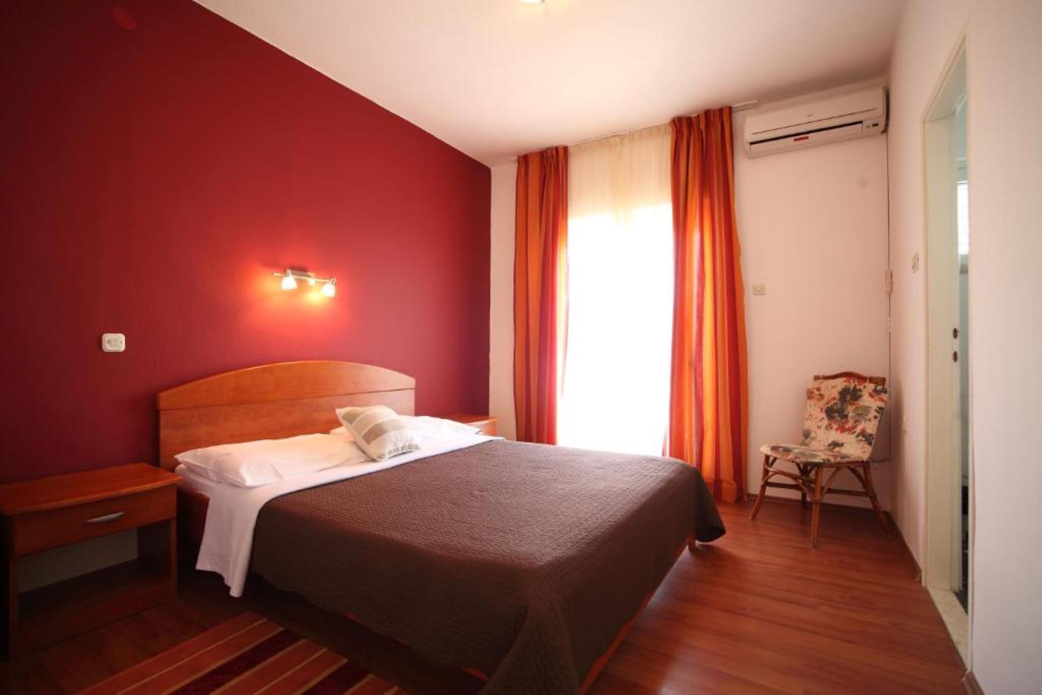 Una camera d'albergo con un letto, un comodino, una sedia, una finestra con tende e un condizionatore d'aria.