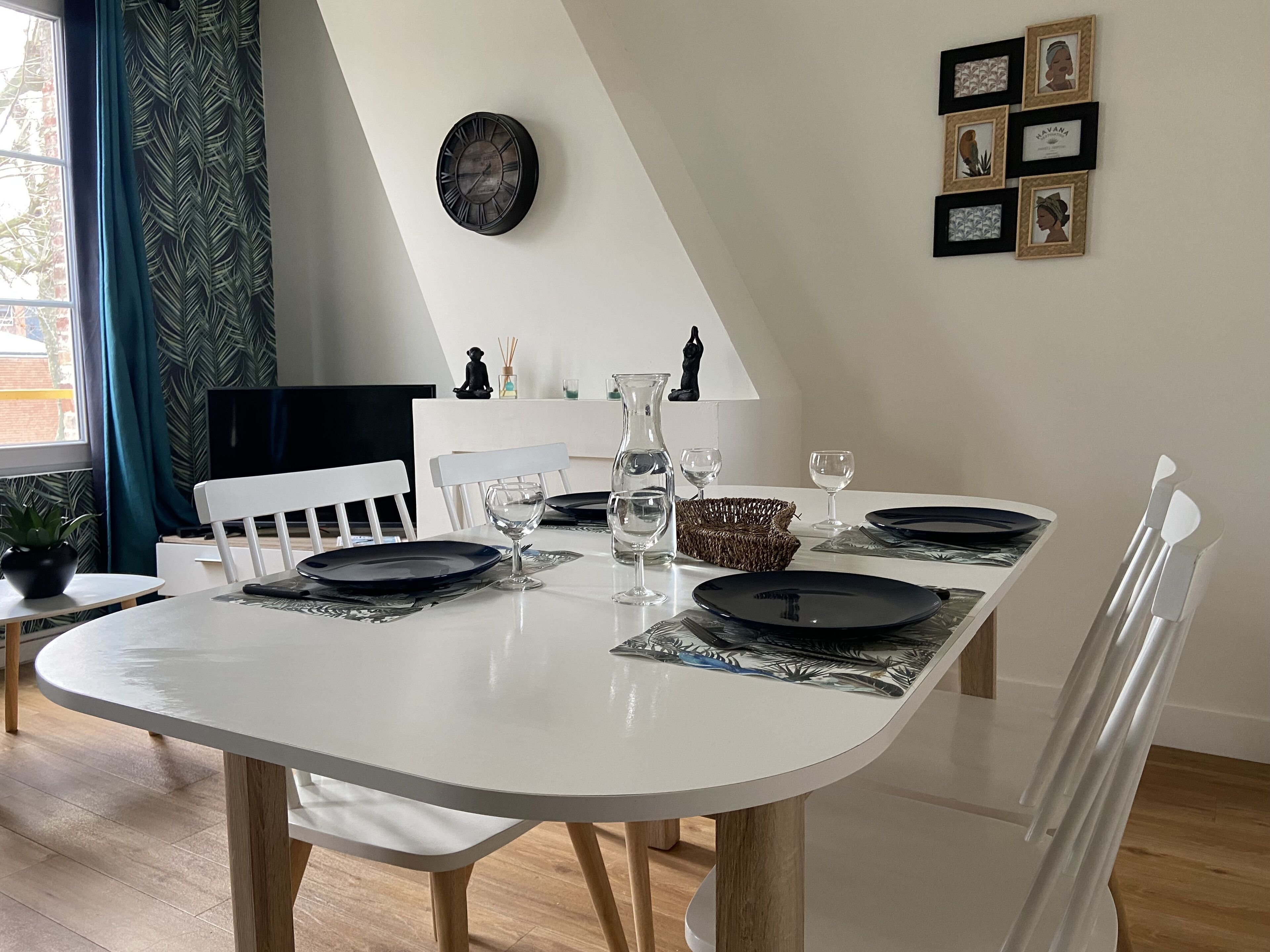 A dining area with a white table set for four, featuring black plates and clear glasses.