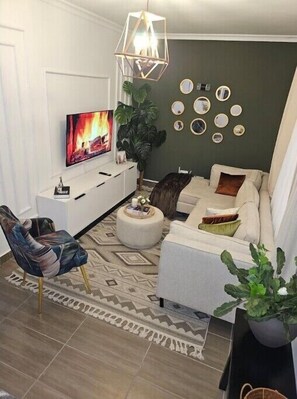 A living room with a TV, sofa, chair, and decorative wall art. - Larka Haven (Ruaka)