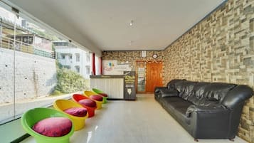 A hotel lobby with a black leather sofa, colorful chairs, a reception desk, and a patterned wall.