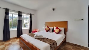 A hotel room with a large bed, a bedside table, a window with curtains, and a view of the outdoors.