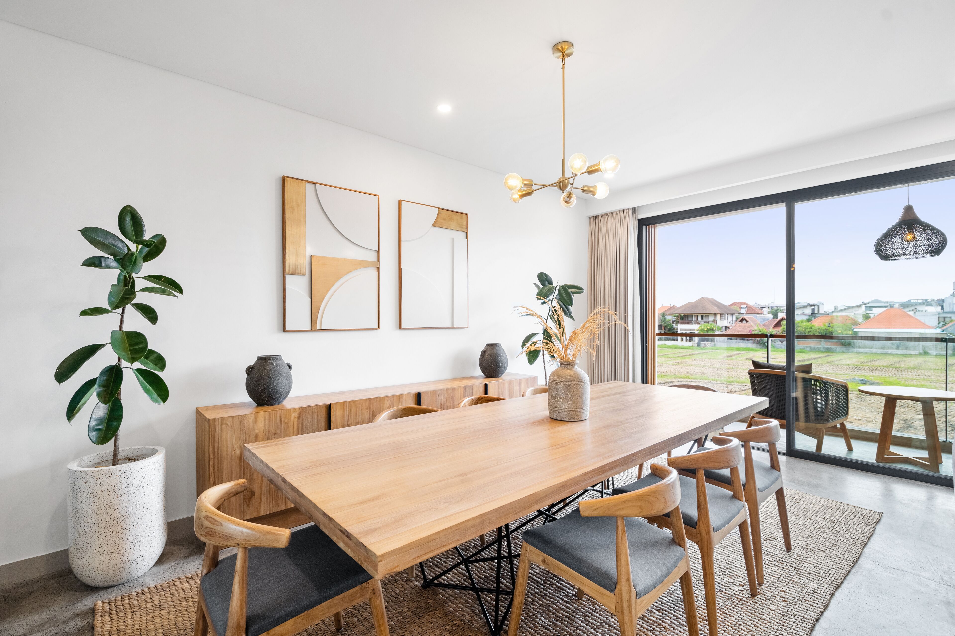 A modern dining area with a wooden table and chairs, a large potted plant, and artwork on the wall.
