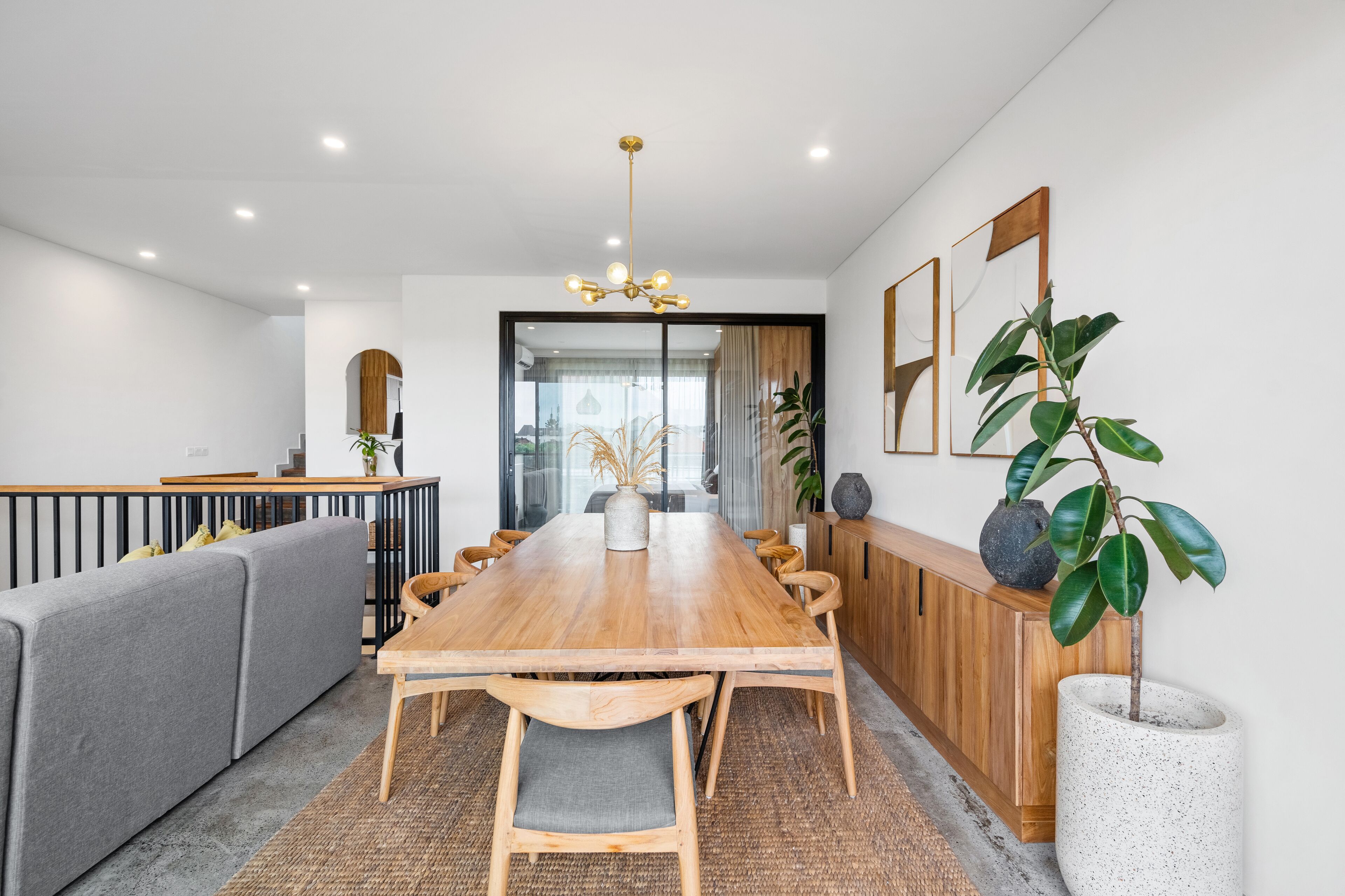 Un comedor moderno con una mesa de madera, un sofá gris y un armario de madera.