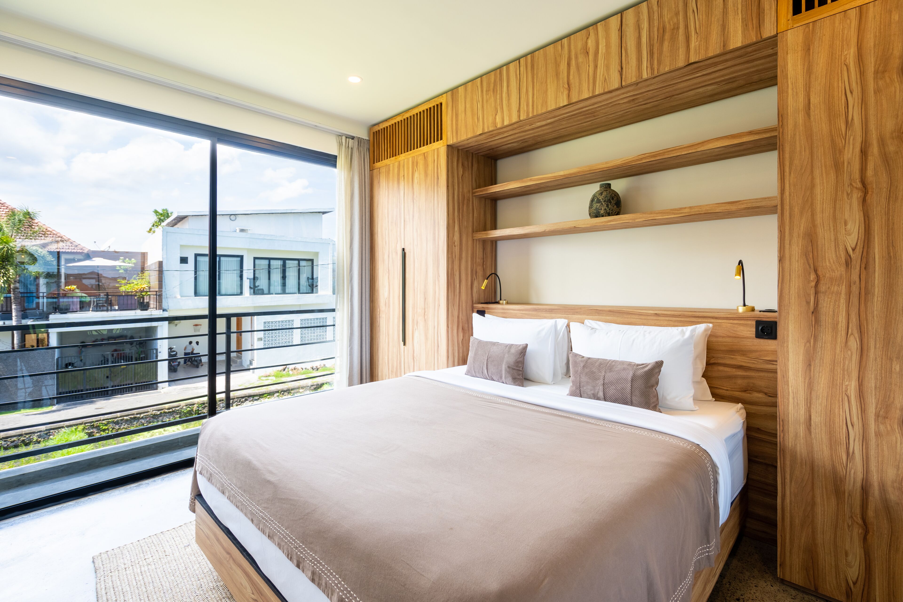 A modern bedroom with a large bed, wooden headboard, and built-in shelves.