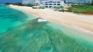 Een hotel aan het strand met meerdere gebouwen, een zandstrand en helder turquoise water.
