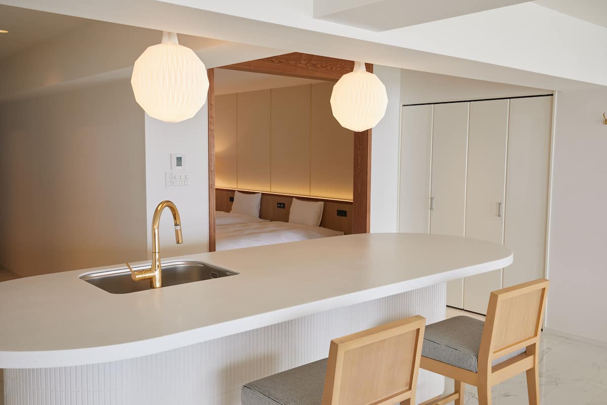 A modern kitchen with a white countertop, gold faucet, and two pendant lights.