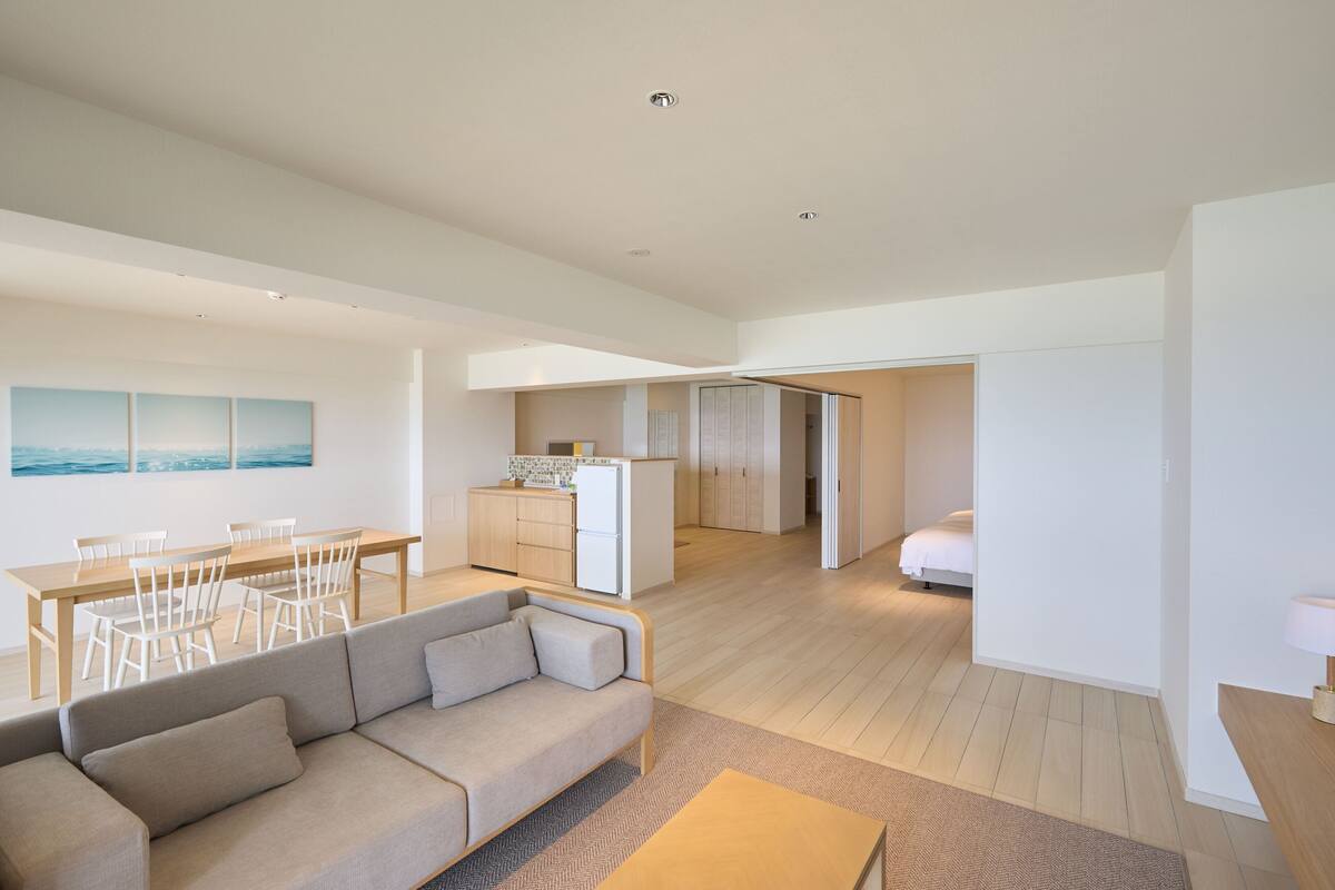 A spacious living area with a sofa, dining table, and chairs, a kitchenette, and a bedroom with a bed.