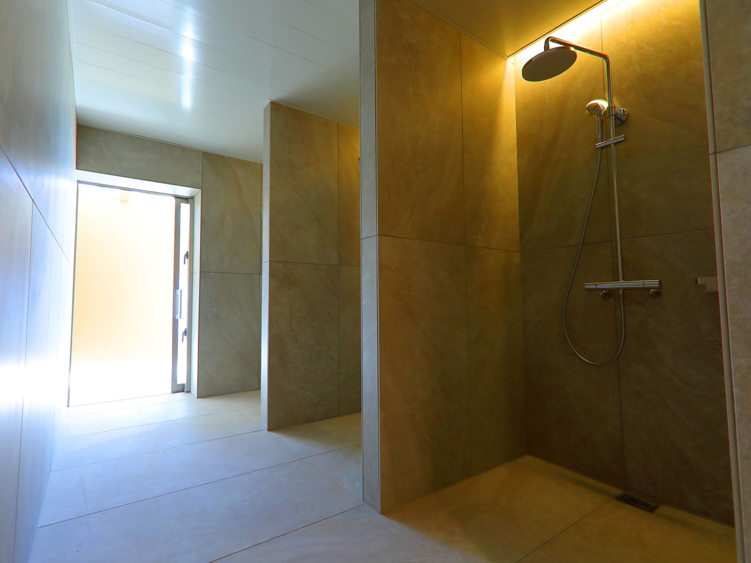 A modern bathroom with a walk-in shower, tiled walls, and a door leading to another room.