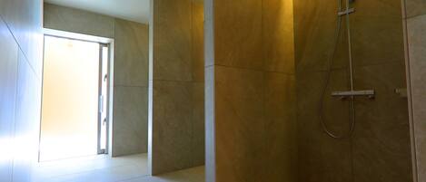 A modern bathroom with a walk-in shower, tiled walls, and a door leading to another room.