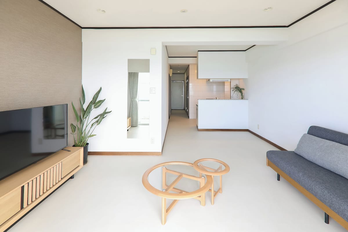 A modern living room with a flat-screen TV, a sofa, two wooden side tables, and a potted plant.