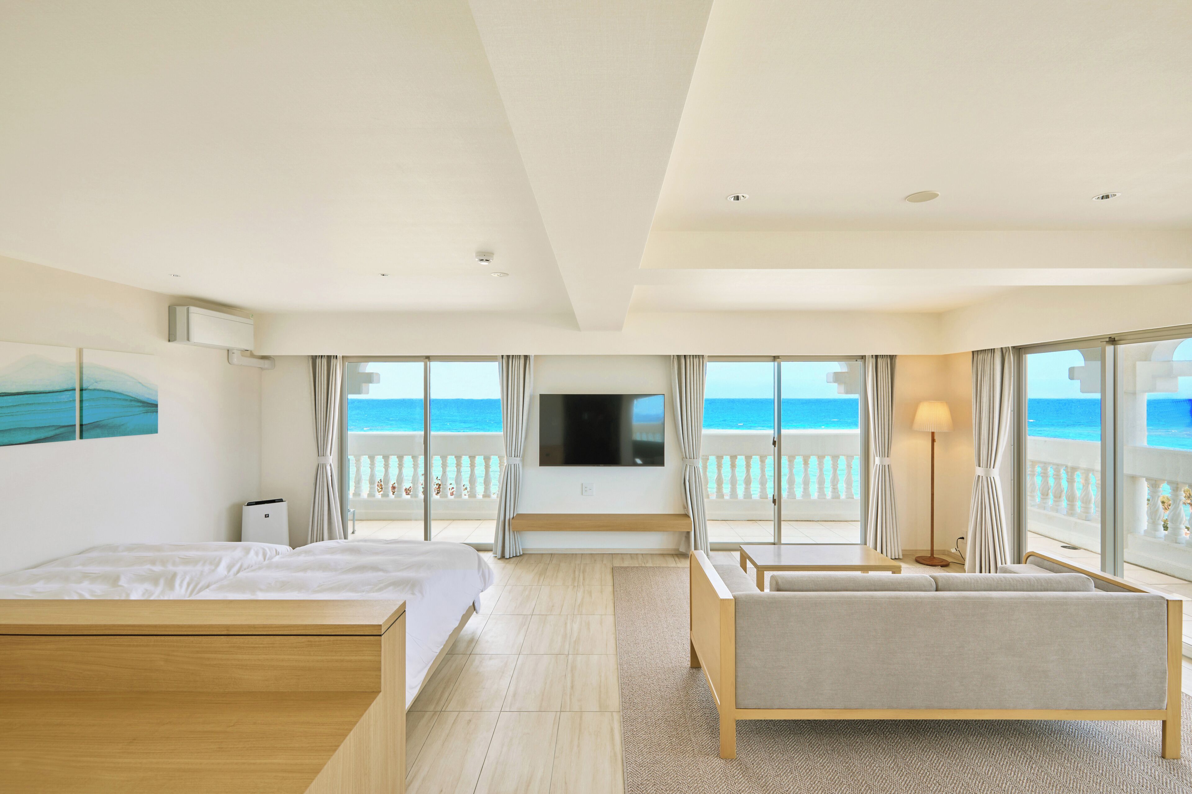 A hotel room with a bed, a sofa, a TV, and a balcony with a view of the sea.