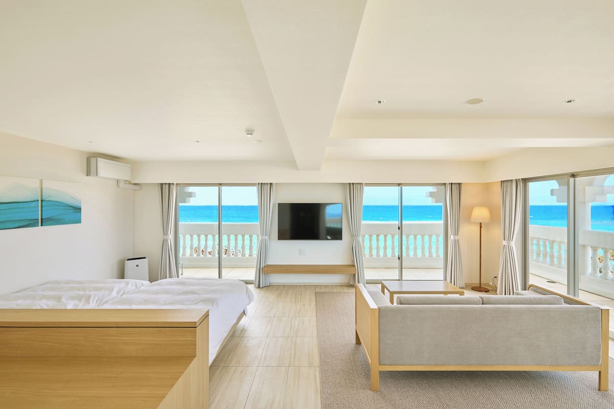 A hotel room with a bed, a sofa, a TV, and a balcony with a view of the sea.