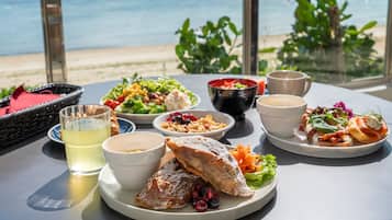 A table with various dishes and drinks, overlooking a beach and ocean view.