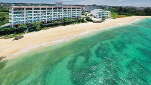 Een strandhotel met meerdere verdiepingen, een zandstrand en helder turquoise water.