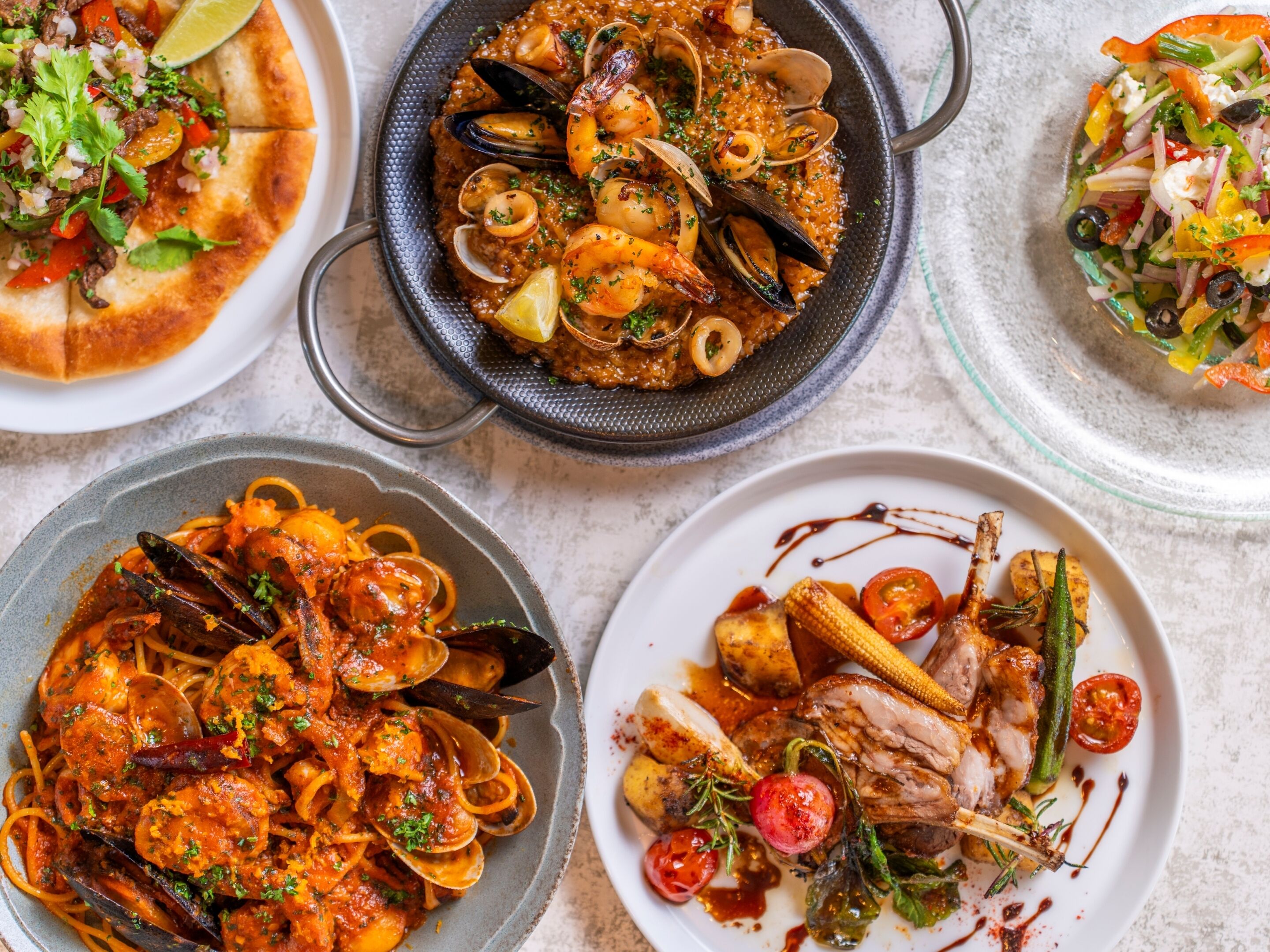 Diversos platos de mariscos, como mejillones, camarones y pasta, presentados en distintas vajillas.
