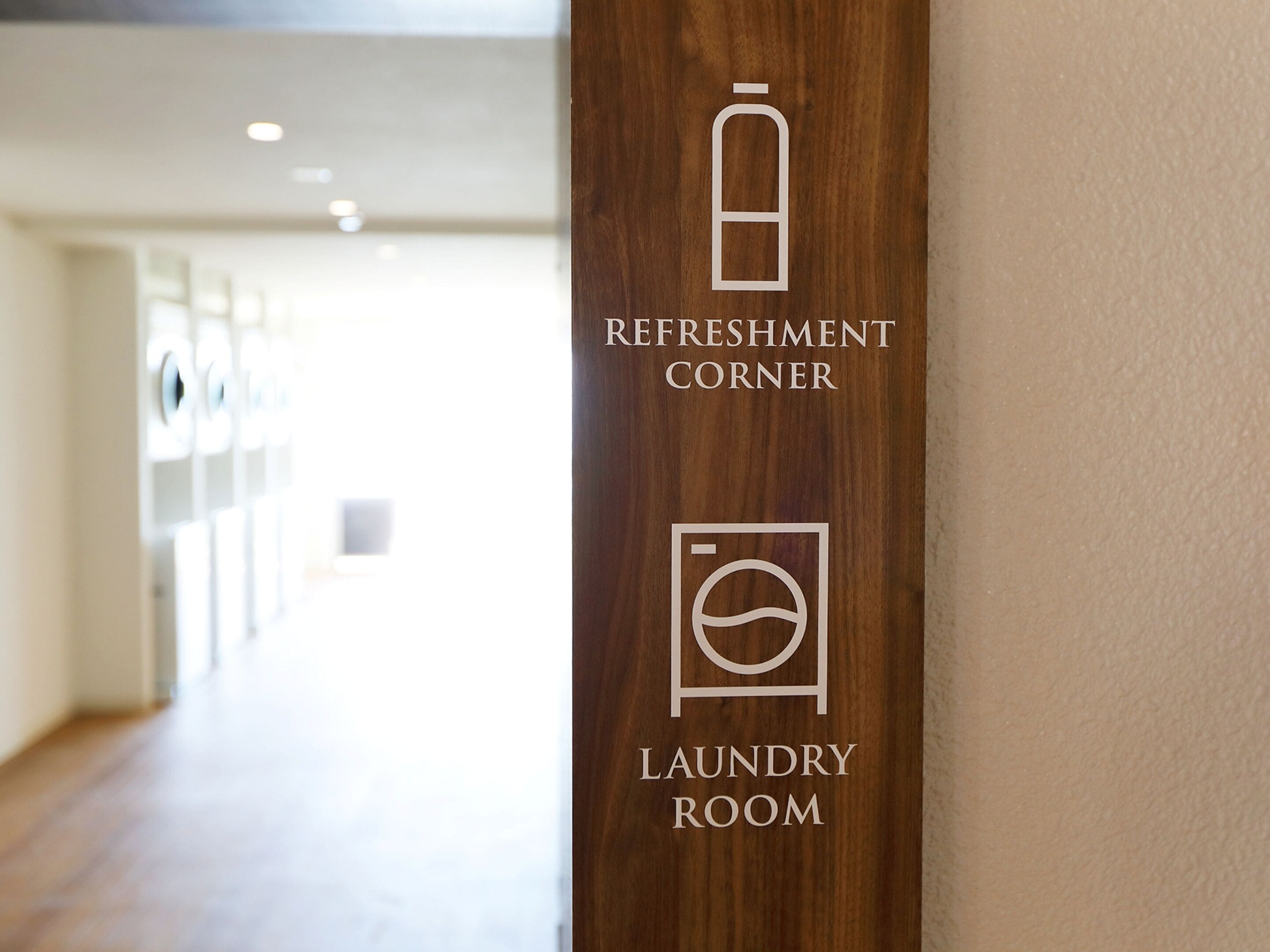 A hallway with a wooden pillar displaying icons for a refreshment corner and a laundry room.