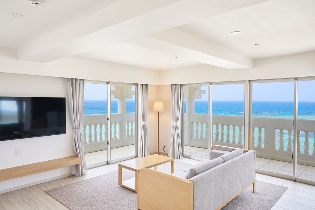 Habitación de hotel moderna con un televisor grande, un sofá, una mesita y un balcón con vistas al océano.