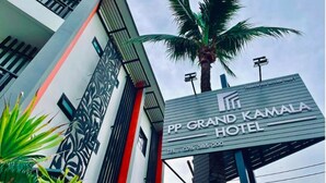 Exterior del hotel PP Grand Kamala, con un letrero llamativo, una palmera y un diseño arquitectónico moderno.