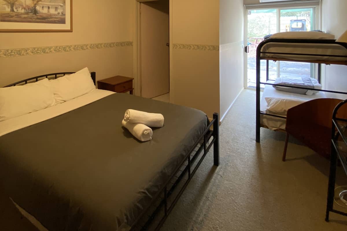 Une chambre avec un lit superposé, un lit simple avec des oreillers, un tableau encadré au mur et une fenêtre avec un appareil de climatisation.