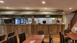 A restaurant with wooden tables and chairs, a counter with a rustic design, and a staircase leading to an upper level.