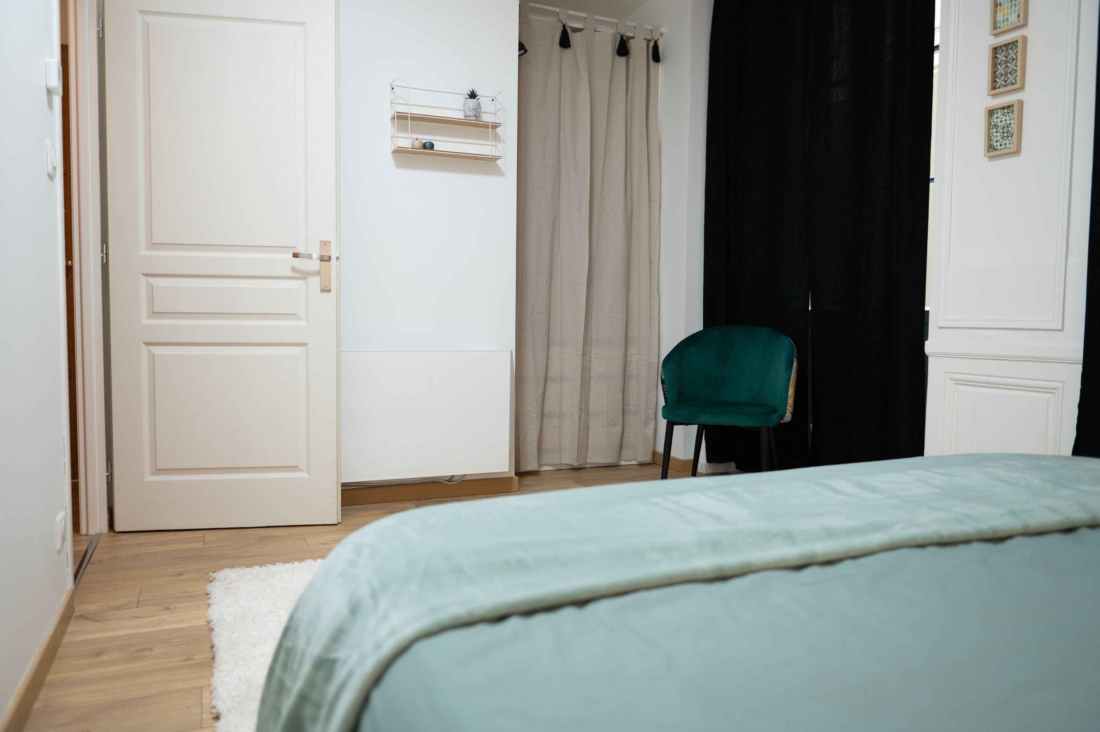 Une chambre à coucher comprenant un lit, une chaise, une porte, une fenêtre avec des rideaux et une étagère ornée d’objets décoratifs.