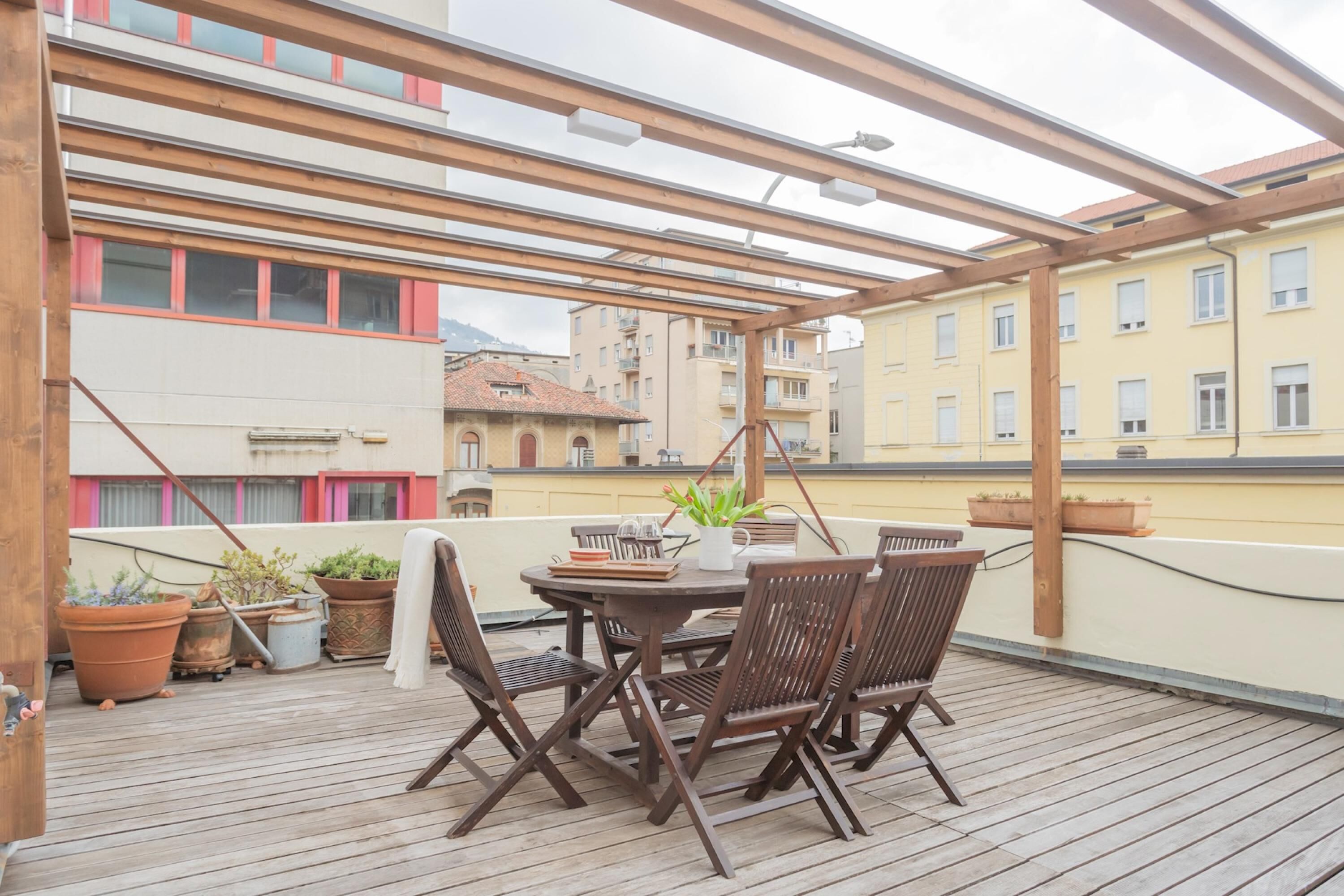 Eine Holzterrasse mit Tisch und Stühlen, umgeben von Topfpflanzen.